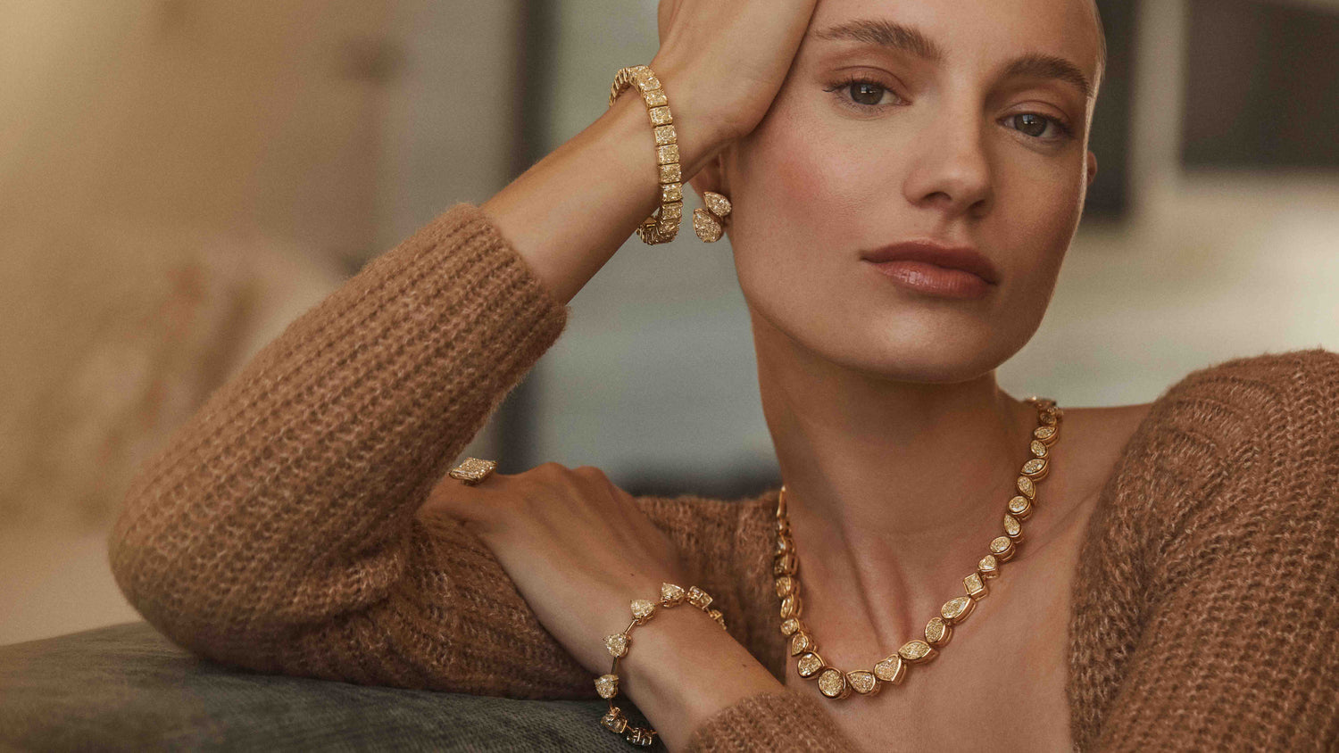 A woman wearing yellow gold mixed shaped yellow natural diamond jewelry in a softly lit setting.