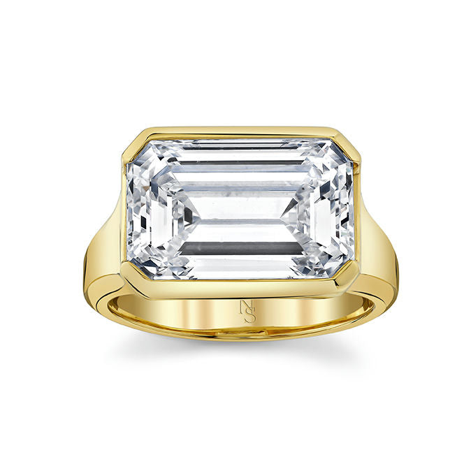 An 18k yellow gold ring with an east-west emerald cut diamond centerpiece.