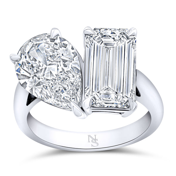 A platinum ring featuring one large emerald cut gemstone and one pear shaped gemstone, with smaller accompanying stones.