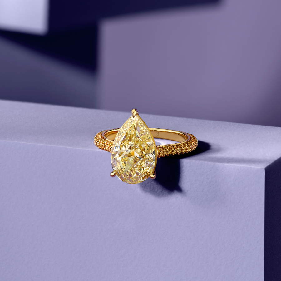 Gold ring with a large teardrop-shaped yellow gemstone on a purple surface