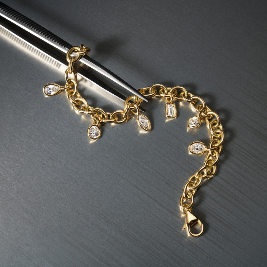 Gold bracelet with mixed shape diamond charms on a dark surface